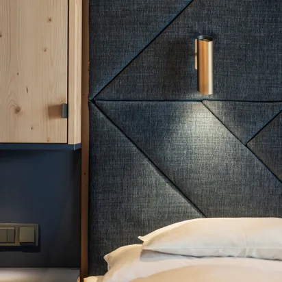Modernes Hotelzimmer mit gepolstertem dunklem Stoffkopfteil und integrierter Leselampe